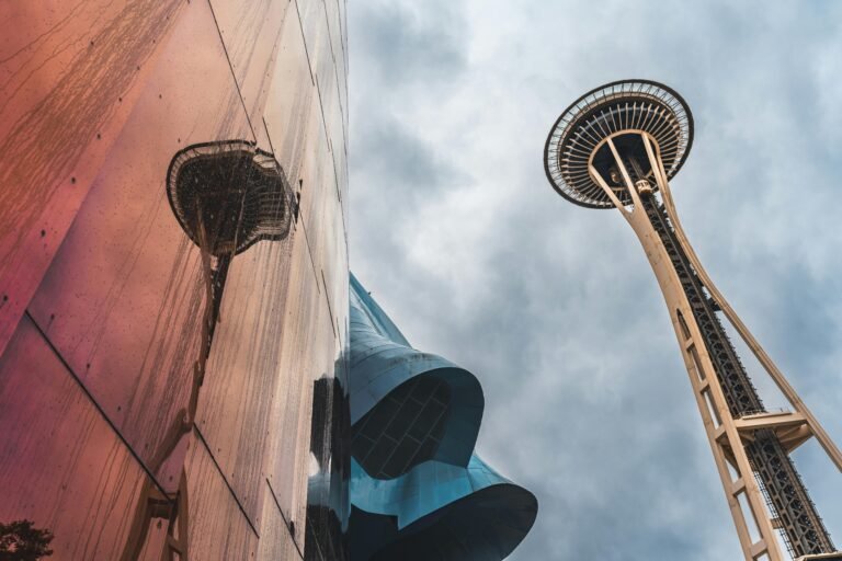 The Space Needle in Seattle reflected on a modern building with an overcast sky.